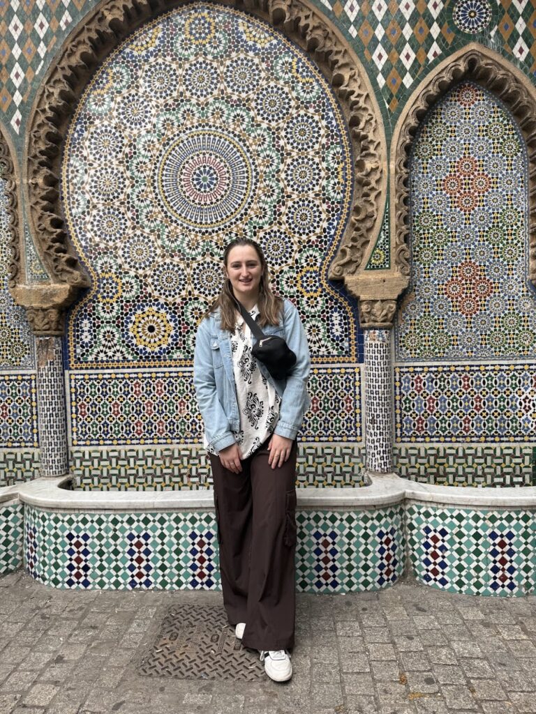 Kayla Nemirovsky from UMBC stands in a jean jacket in front of an ornate wall in Morocco 