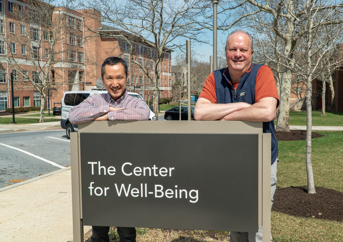 Two men lean against sign that reads "The Center for Well-Being"