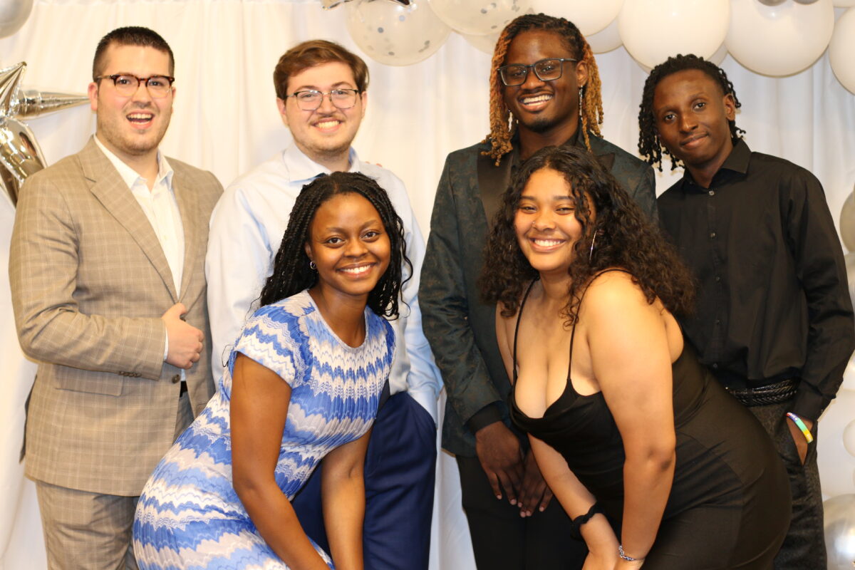 Six people posing for a picture in front of balloons.