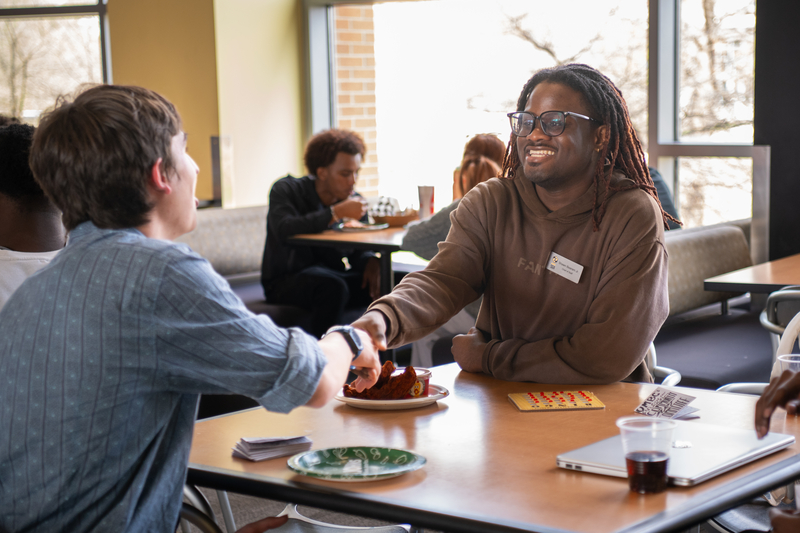 Two people sitting at a table, shaking hands. 