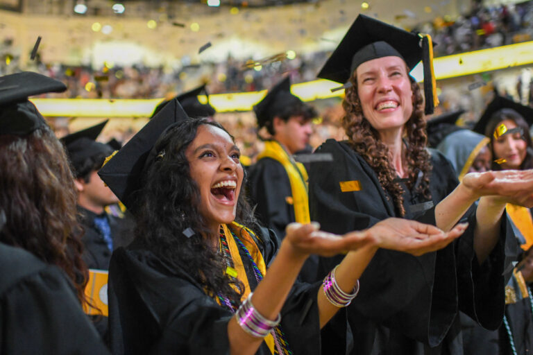 graduates in regalia catch confetti as it comes down from the ceiling