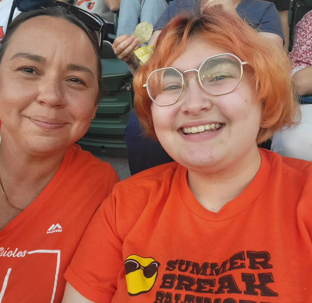 Two students smile for a photo wearing orange shirts