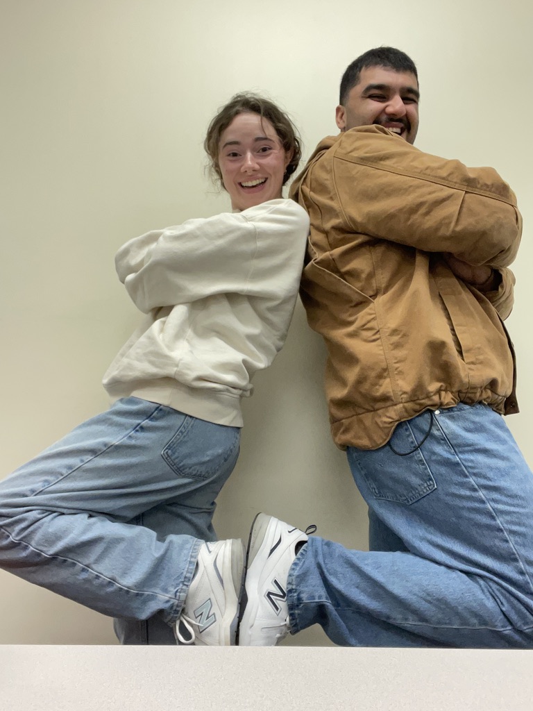 Two students stand back to back with their feet up and touching 