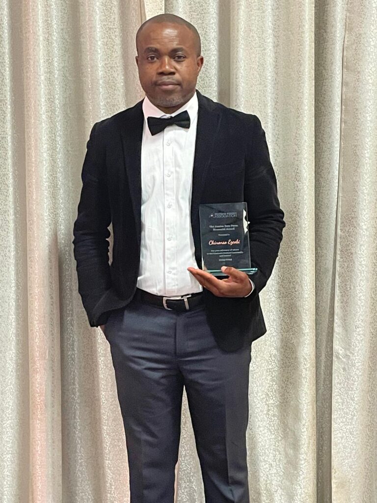 A man stands in a suit holding a glass award and presents himself as a mentor to others
