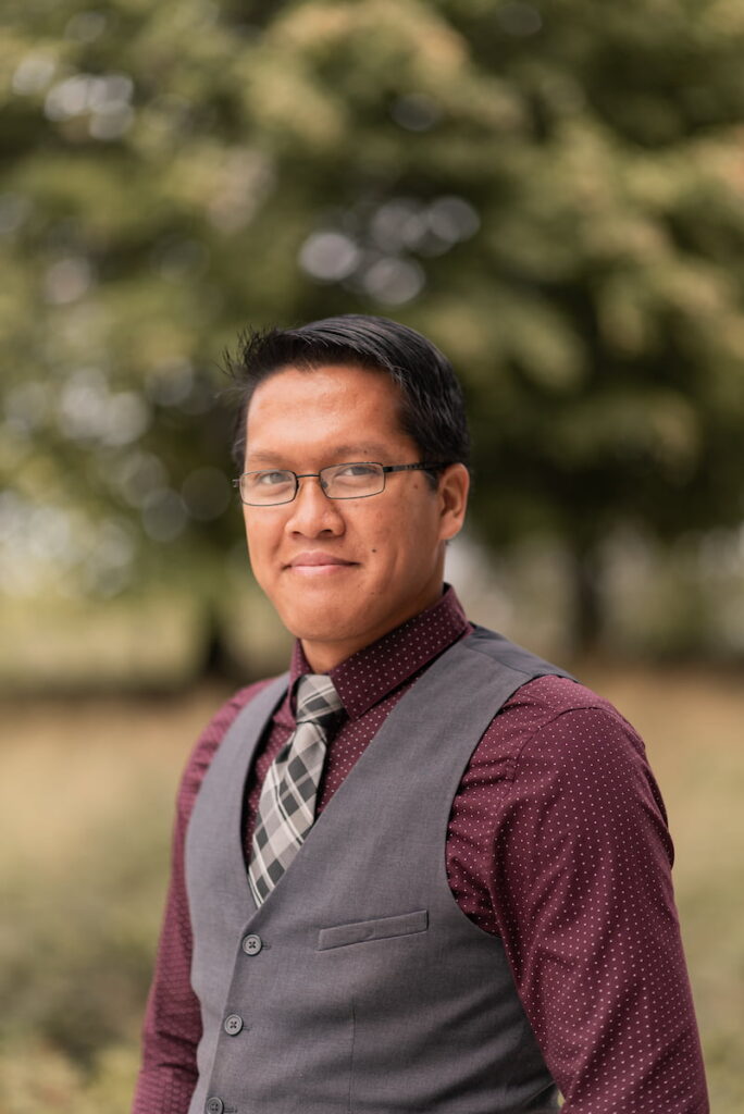 Headshot of a person wearing glasses, a gray vest, and a patterned tie.