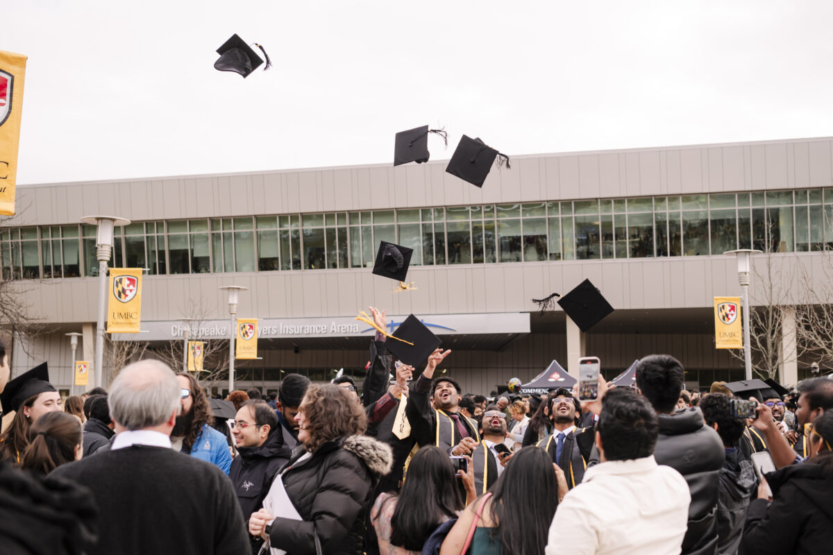 large crowd in commencement regalia, students throwing their caps in the air