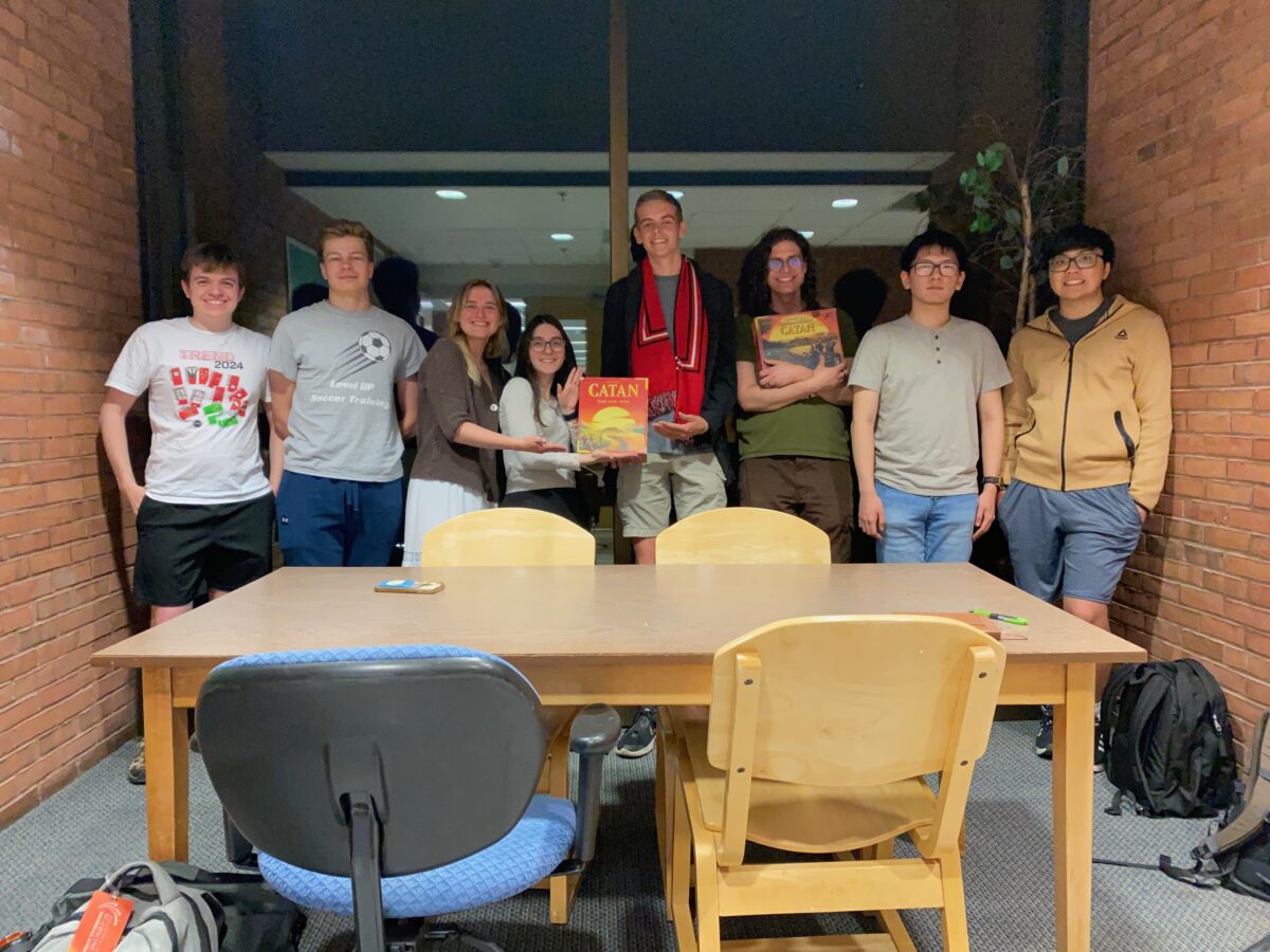 Rileigh Mansfield and her friends standing behind a table; one is holding a Catan board game box