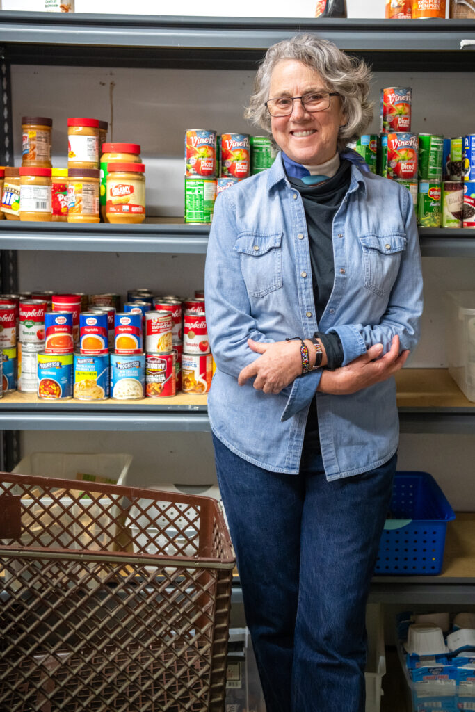 Megan Hamilton, an adult, stands in front of a wall of metal shelves filled with canned good in SWES Shriver Center
