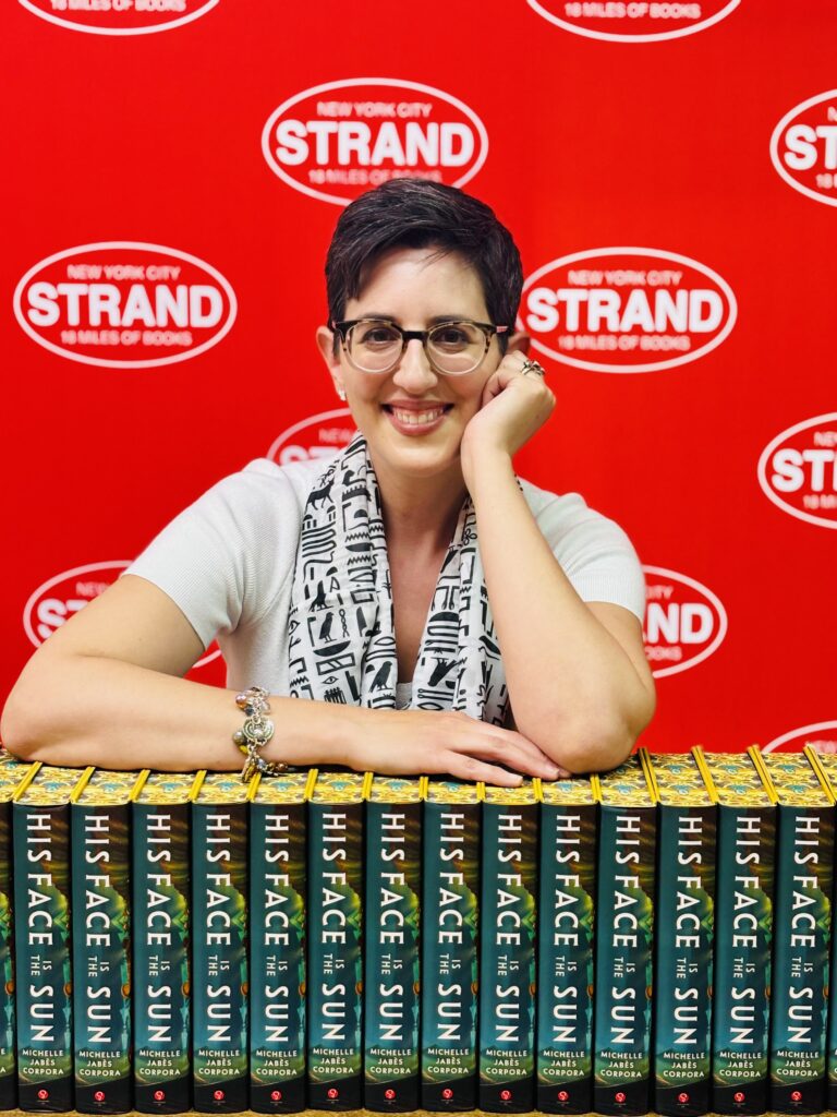 New York Times Bestseller, Corpora, at a book signing event at The Strand Bookstore in New York City. Her arms are leaning against a stack of her books with His face is the sun written across the spines