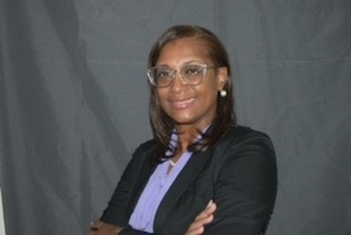 Headshot of a person wearing glasses, a black blazer, and a lavender top with arms crossed.