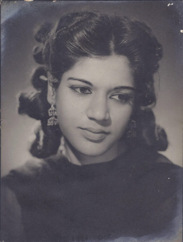 A black and white headshot of a young Indian women, her hair set in curls, she looks to her left