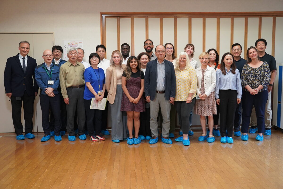 22 people including Alfred Boakye and other gerontology doctoral students, professors, and senior citizens stand together for a group picture. All of them are wearing blue, plastic foot booties.