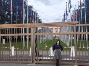 College student, Magaly Lizama Hernandez, a Bernard L. Berkowitz Memorial Award recipient, stands in front of a tall steel door that guards a government building in Switzerland with two rows of flags from around the world in front