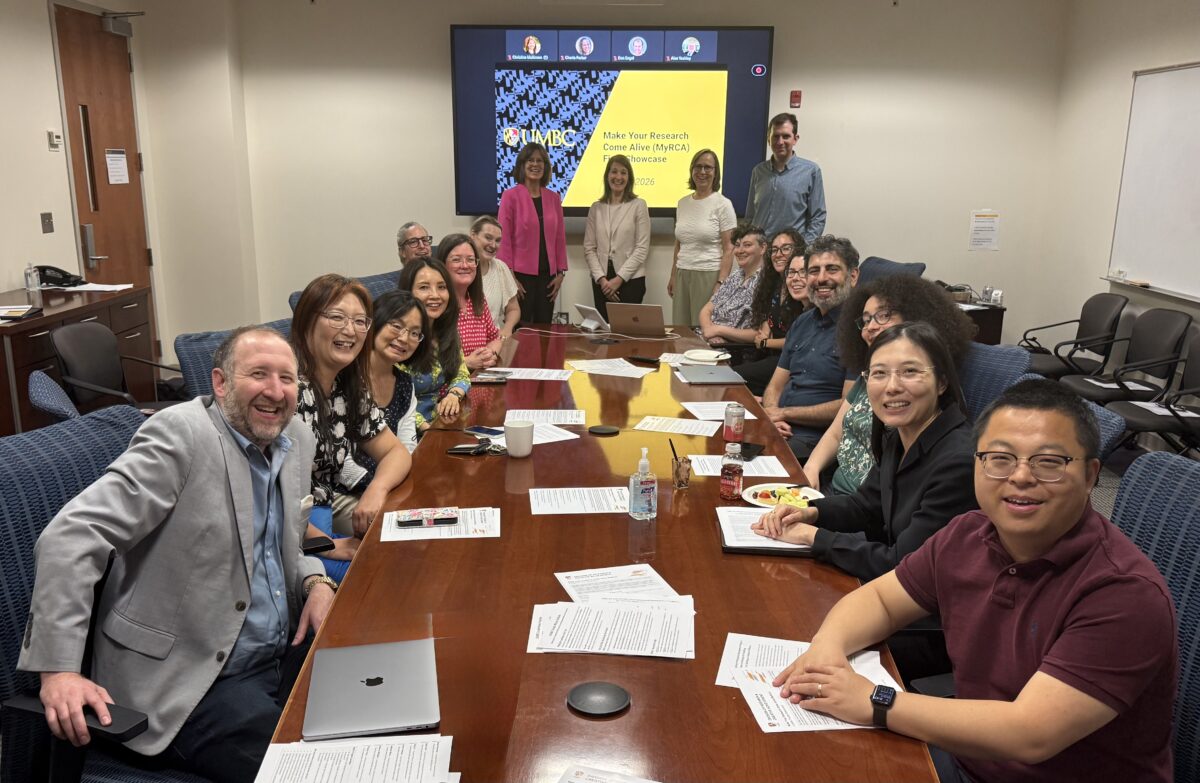 group photo of people sitting around a conference room table with a screen in the front