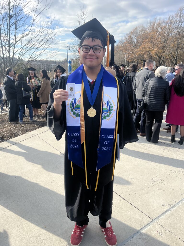A college student wearing his graduation black cap and gown with a blue and white stole with flag of El Salvador