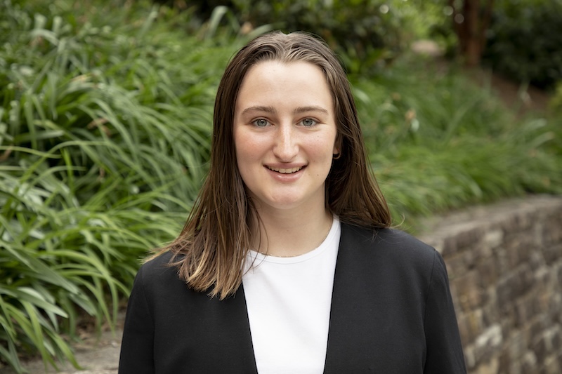 headshot of Kayla Nemirovsky, with shoulder length brown hair and a black blazer on top of a white shirt