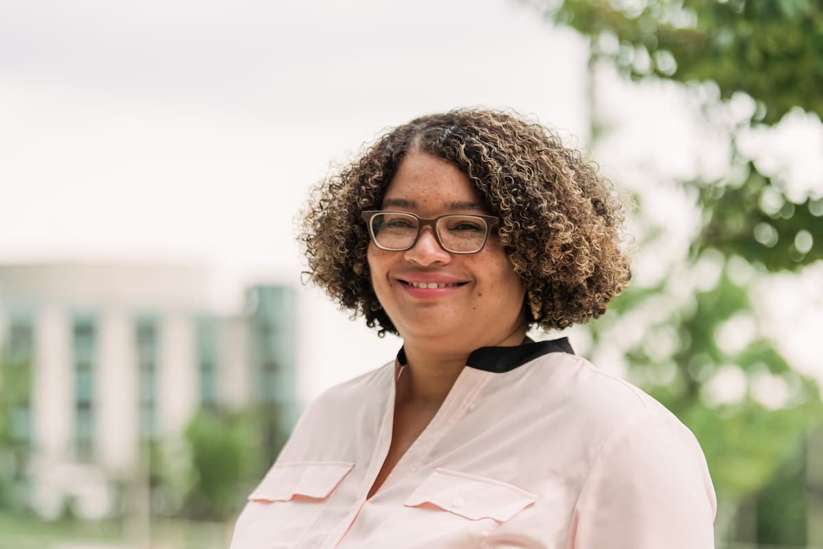 Headshot of a person with curly hair and glasses smiling.