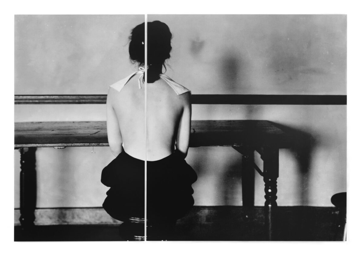 A person viewed from behind sits on a stool at a table.