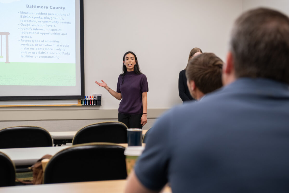 A student researcher points to a presentation slide in front of a classroom