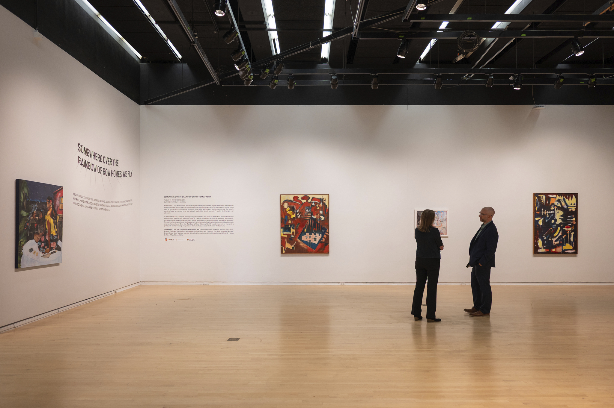 Two people stand in an art gallery looking at artworks hung on white walls.