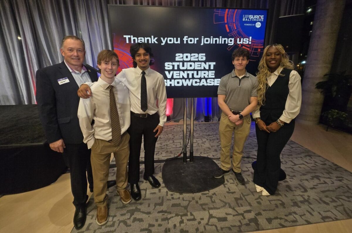 group photo of Kevin Fulmer with student business award winners Aidan Fleischer, Charles Nerad, Abhinav Patel, and Velma Funebe in front of a screen that reads, "Thank you for joing us! 2026 Student Venture Showcase"