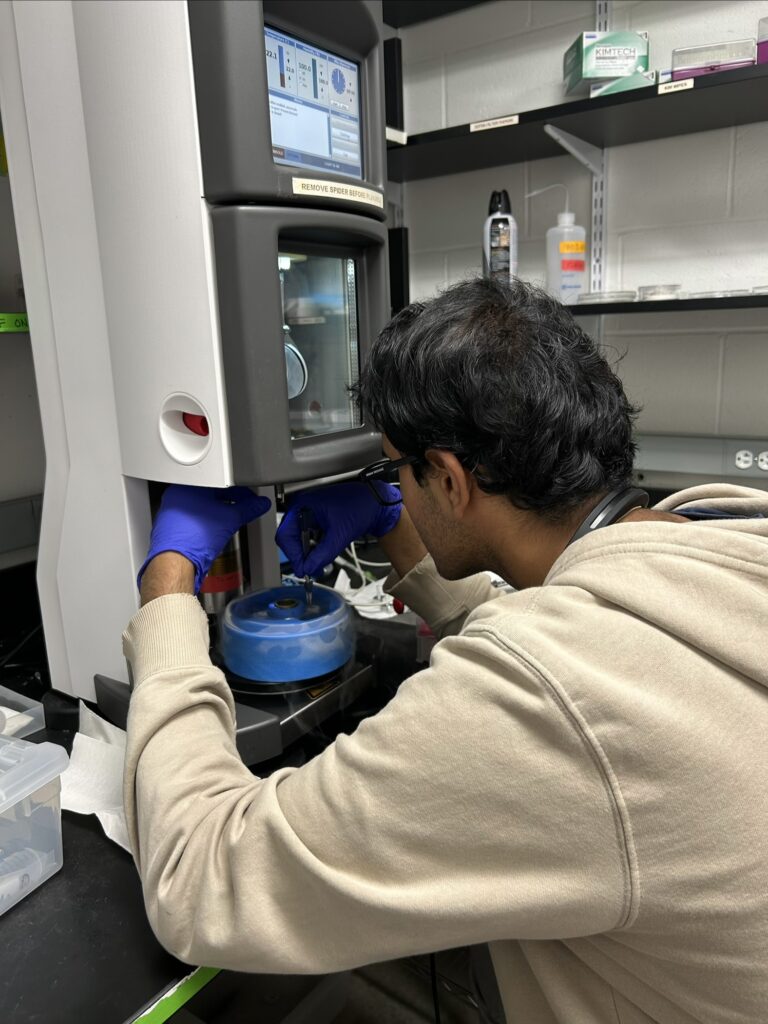 Cech Fellow Aryan Srivastava in a lab coat looking into a microscope