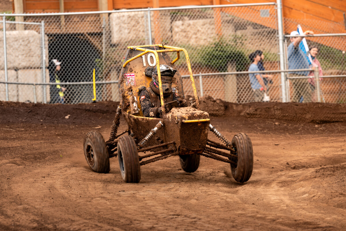 Off-road Baja car covered in mud drives on a dirt track.