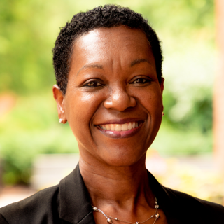 Professional portrait of Yvette Mozie-Ross, standing outside, wearing a black blazer and smiling.