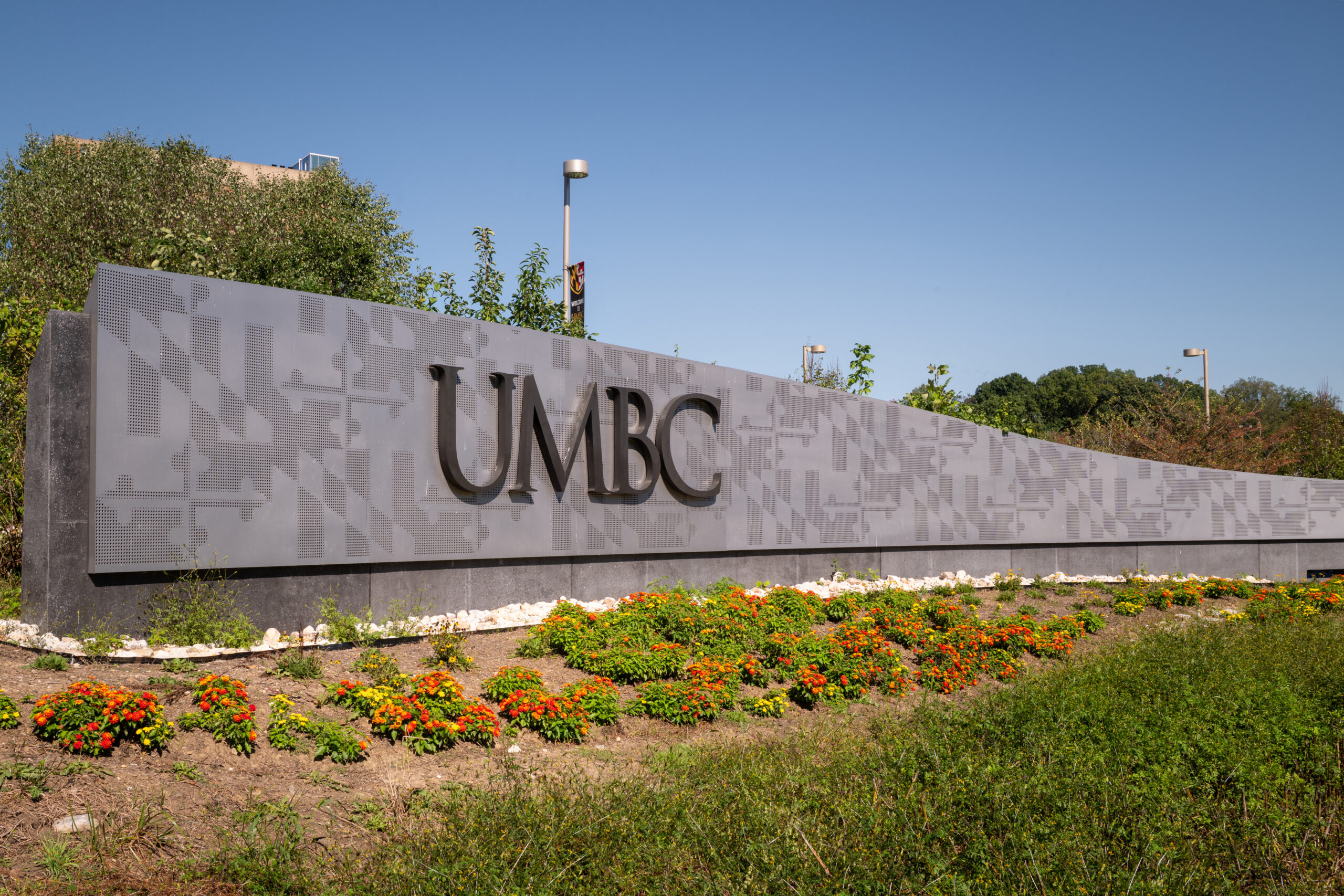 "UMBC" on large outdoor sign. Flowers are planted in front of the sign.