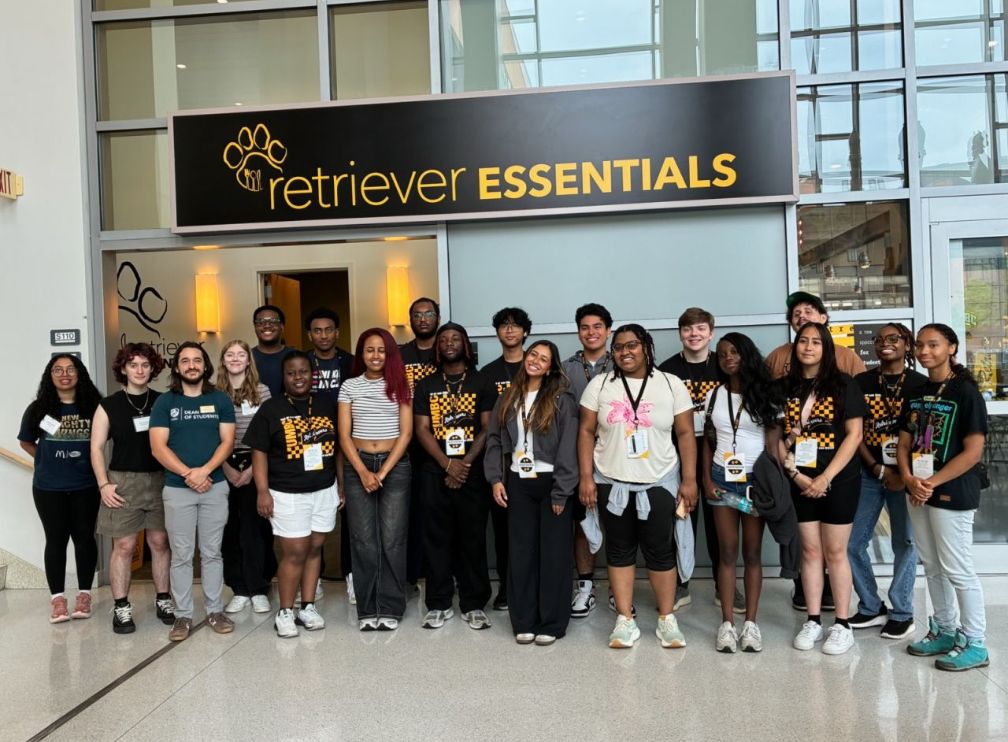 a group of 20 to 30 students stand in front of a sign that says Retriever Essentials