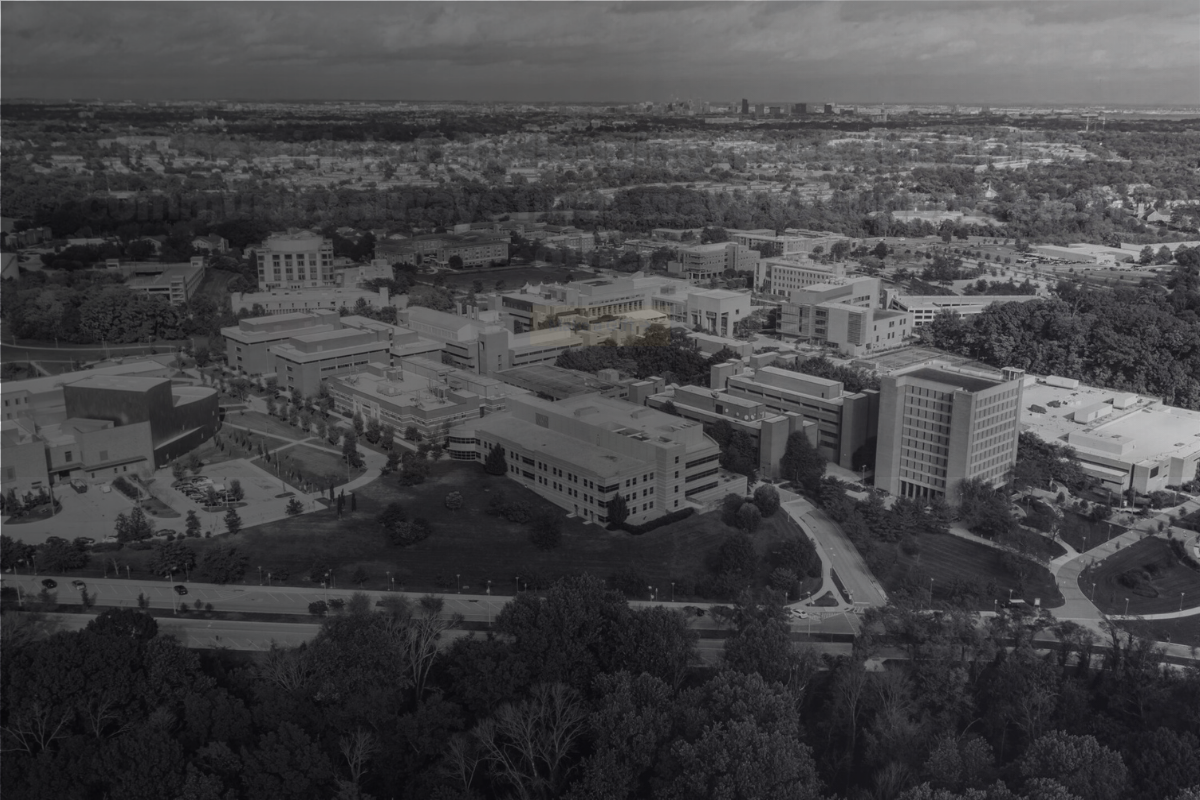 Aerial view of the UMBC campus with academic buildings, roads, and surrounding wooded areas in black and white.