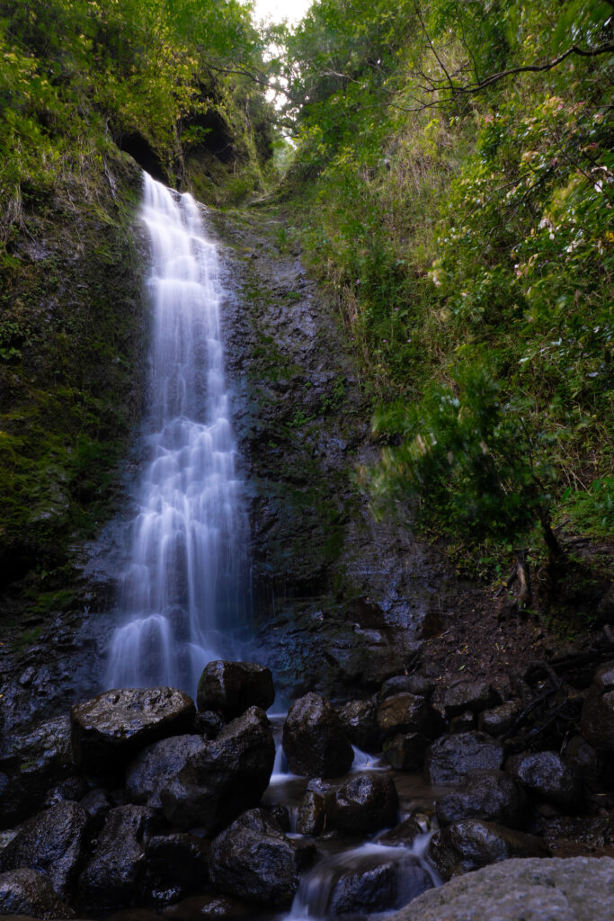 tall waterfall with black rocks at base and green vegetation around