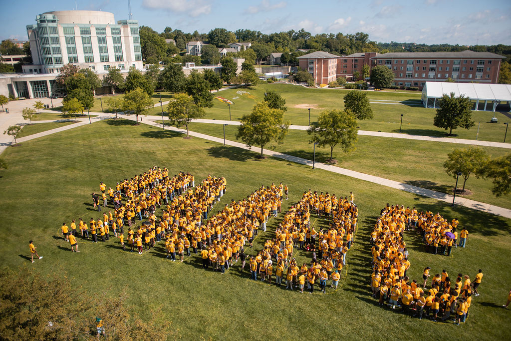 from an aerial perspective, hundreds of students in yellow shirts gather on the university lawn to spell out the letters UMBC