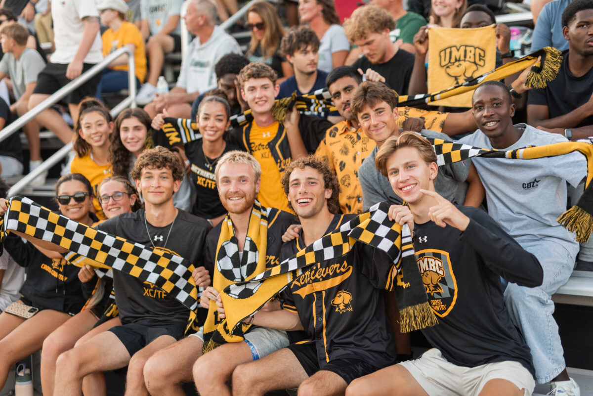 students with a lot of black and gold gear sit in the bleachers to cheer on the Retriever athletics teams and make sure everyone feels like they belong