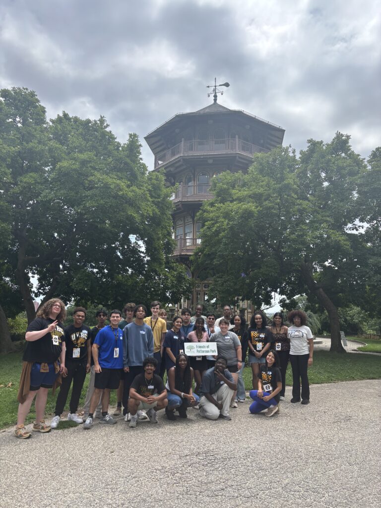 a group of work-integrated learning students gather outside in front of green trees and a large pagoda-like building