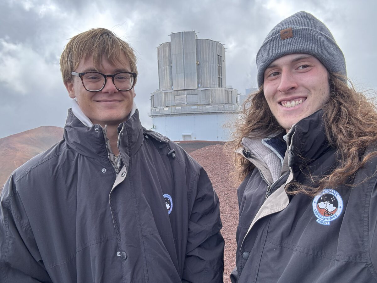 Noah Reichardt and Hyde Kenney stand on a barren landscape, a large observatory behind them
