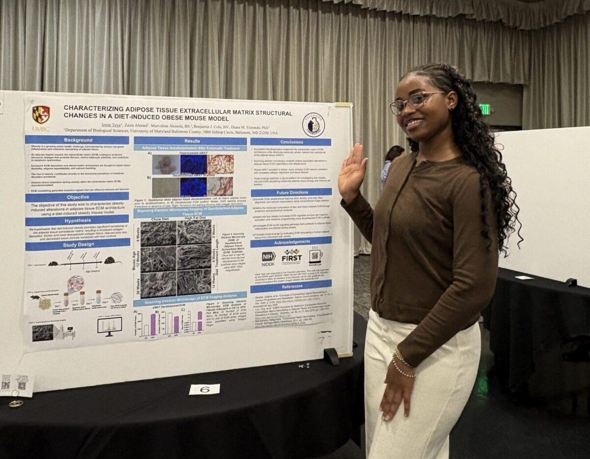 Irene Teye smiles and gestures toward her Summer Undergraduate Research Fest poster, titled, "Characterizing adipose tissue extracellular matrix structural changes in a diet-induced obese mouse model"