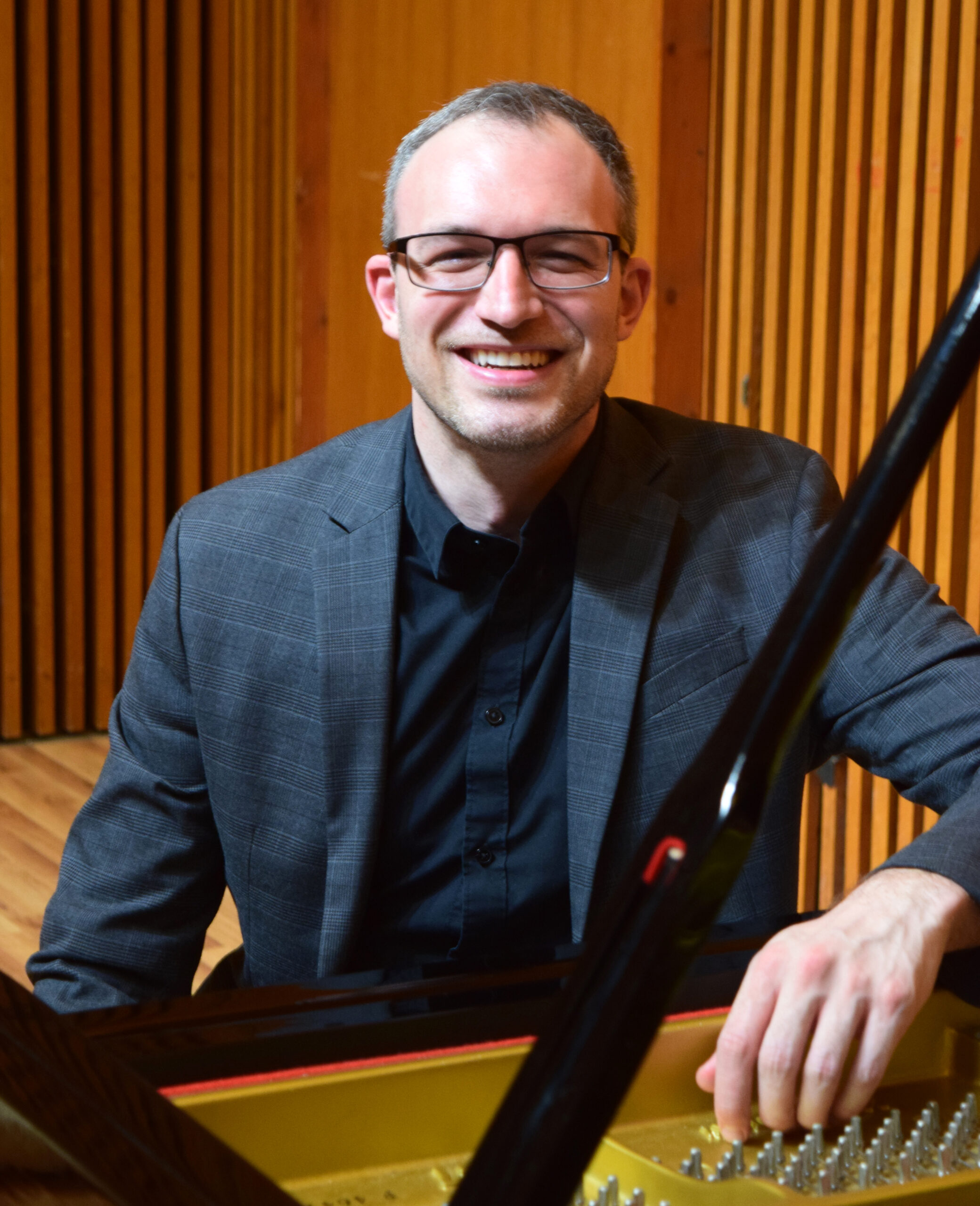 A person smiles while sitting at a grand piano.
