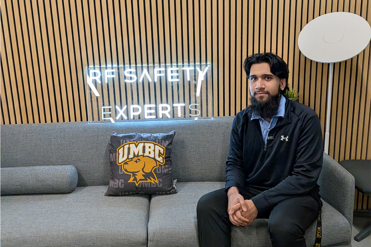 Kaleem Butt sit on a couch in the office, next to UMBC pillow and "RF Safety Experts"neon sign.