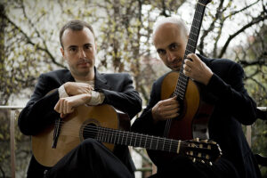 Two people sitting together, each holding a classical guitar.