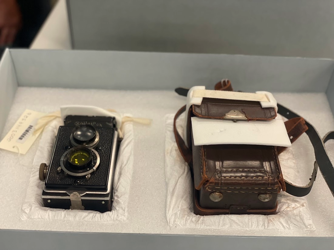 Two WWII hand-held cameras sit inside an archival box