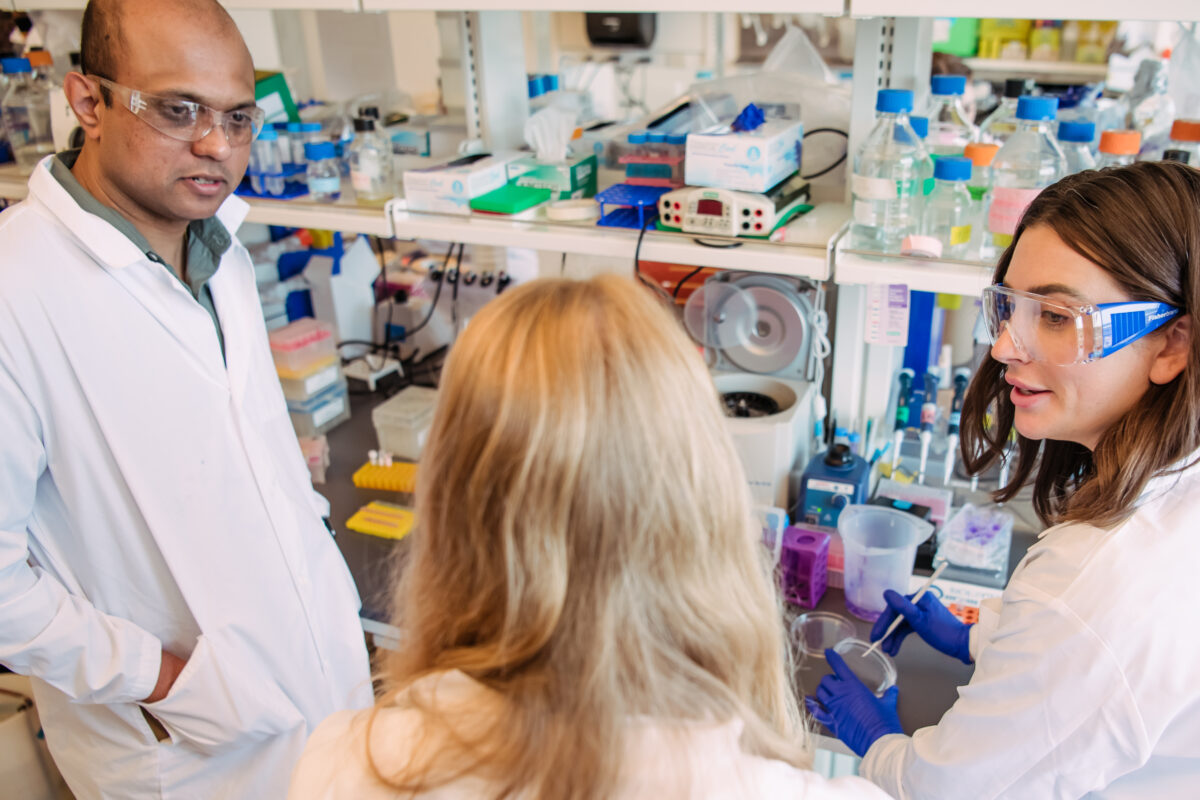 Achuth Padmanabhan and two members of his lab group talk to each other at in the lab where they conduct ovarian cancer research, with colorful lab supplies in the background