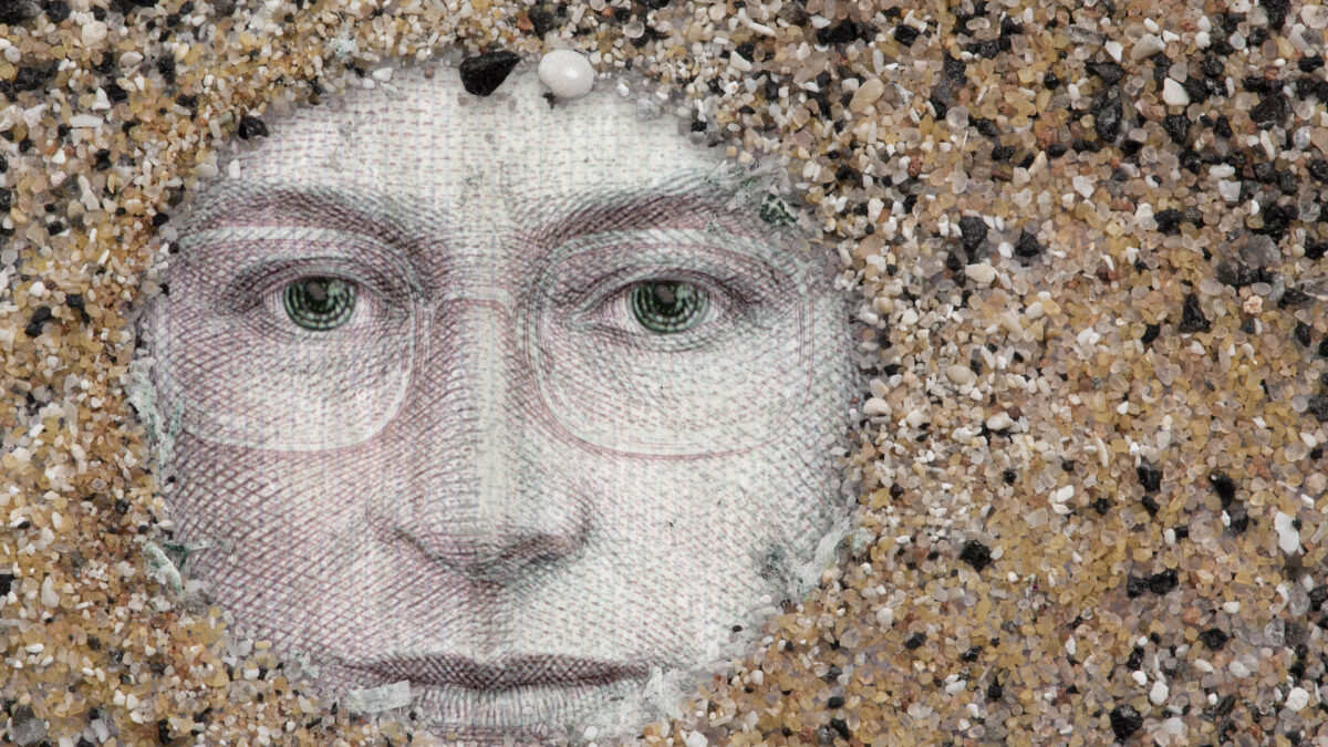 A person's face, as depicted on currency, is in a circle surrounded by grains of sand.
