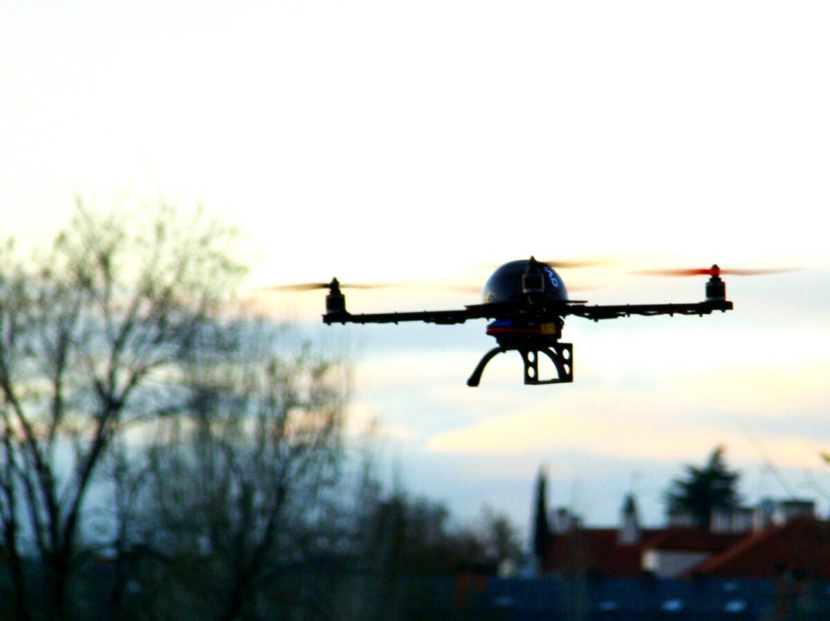 a drone in silhouette flying at twilight, trees in the background