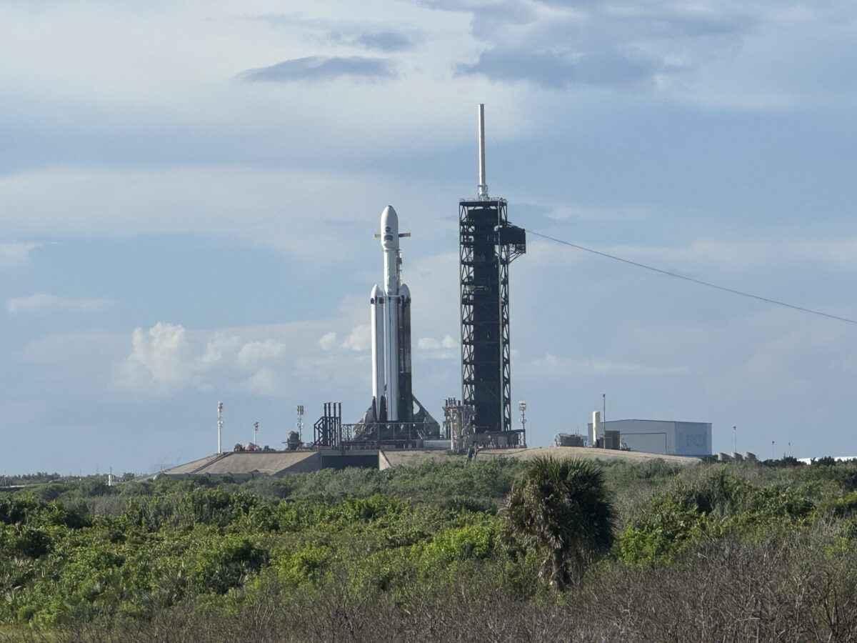 large rocket carrying Roman Telescope visible at a distance across grassy fields