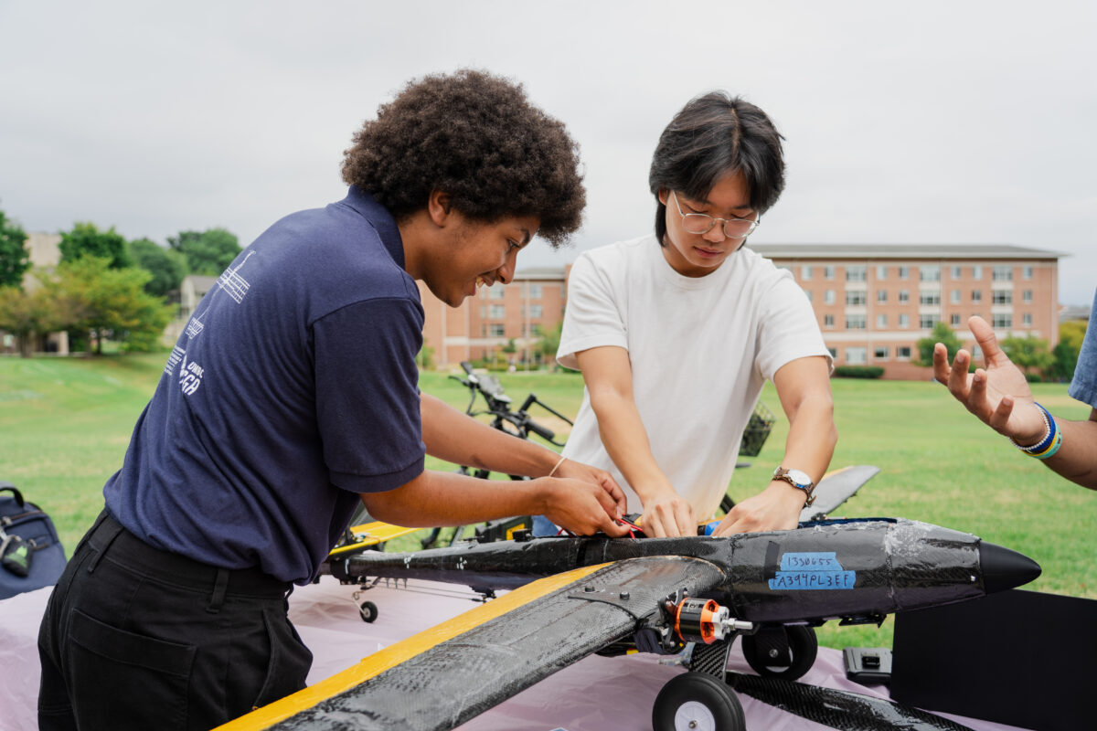 Two college students work on a drone that looks like a small plane