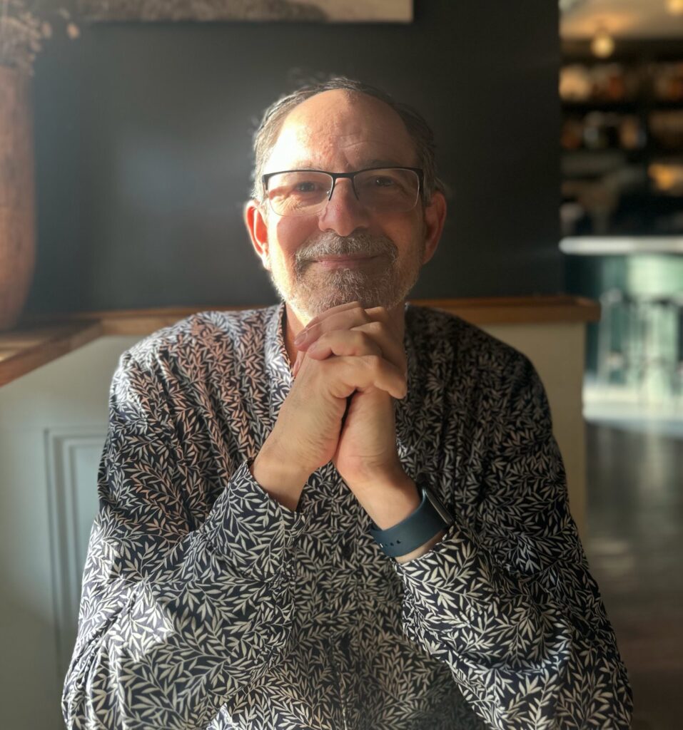 Headshot of Craig Saper, author of a book about small presses, sits with his hands crossed in front of him.