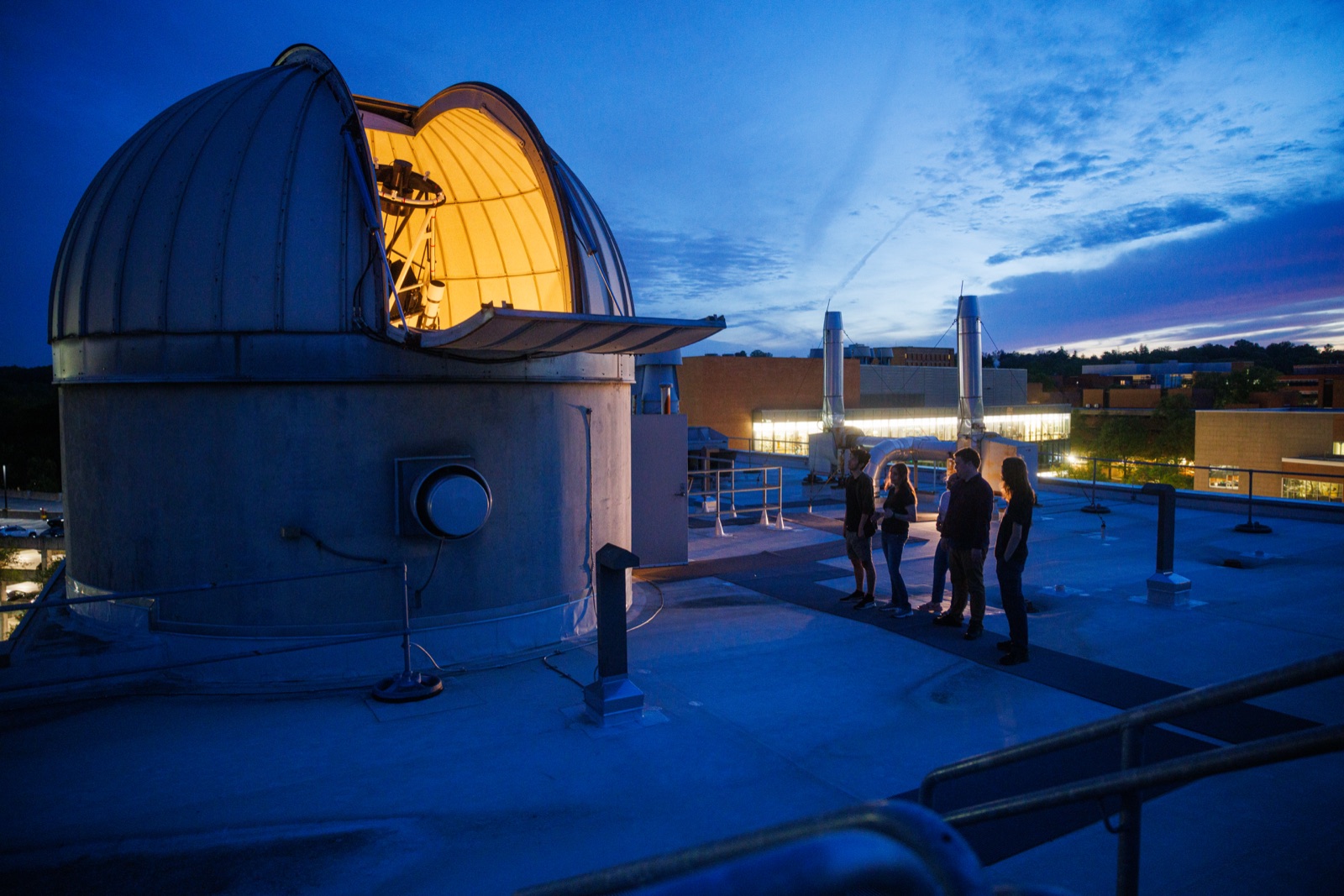 Students on the rooftop beside the glowing UMBC observatory dome at dusk