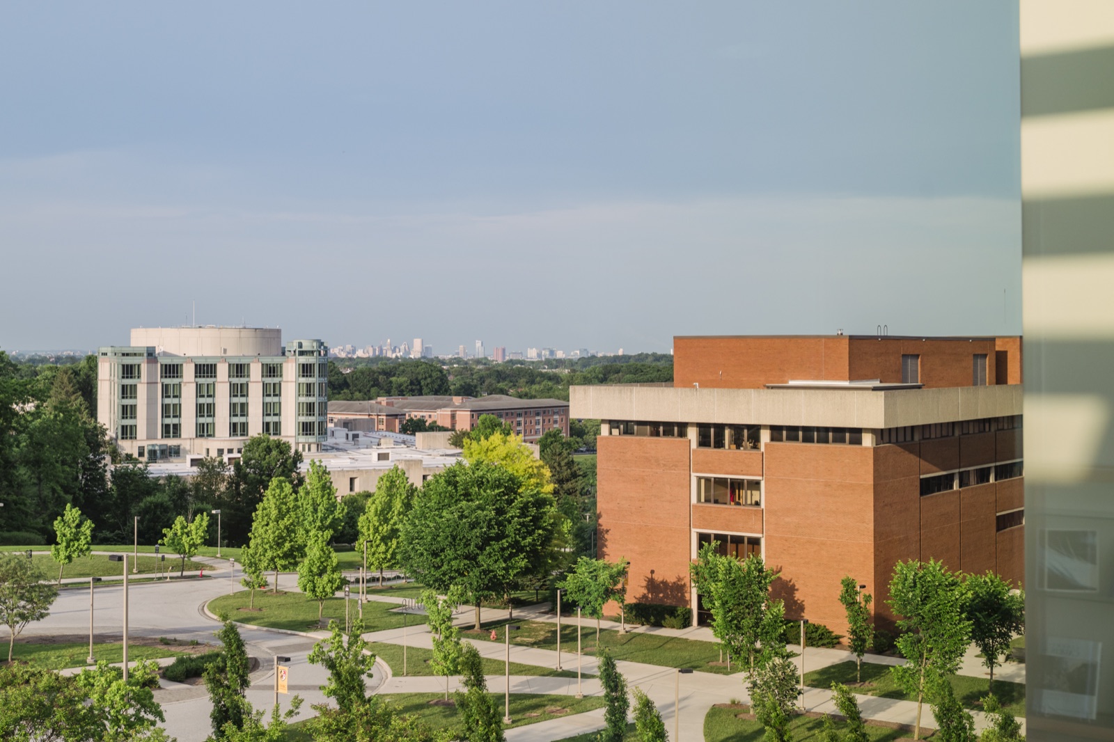 UMBC campus buildings among green summer trees, with the Baltimore skyline on the horizon