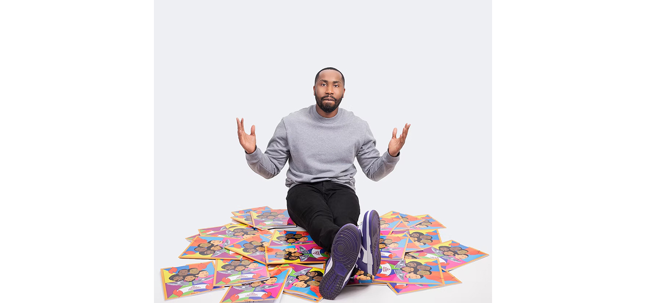 A person sits on the floor with hands raised, surrounded by numerous copies of a colorful, illustrated book cover.